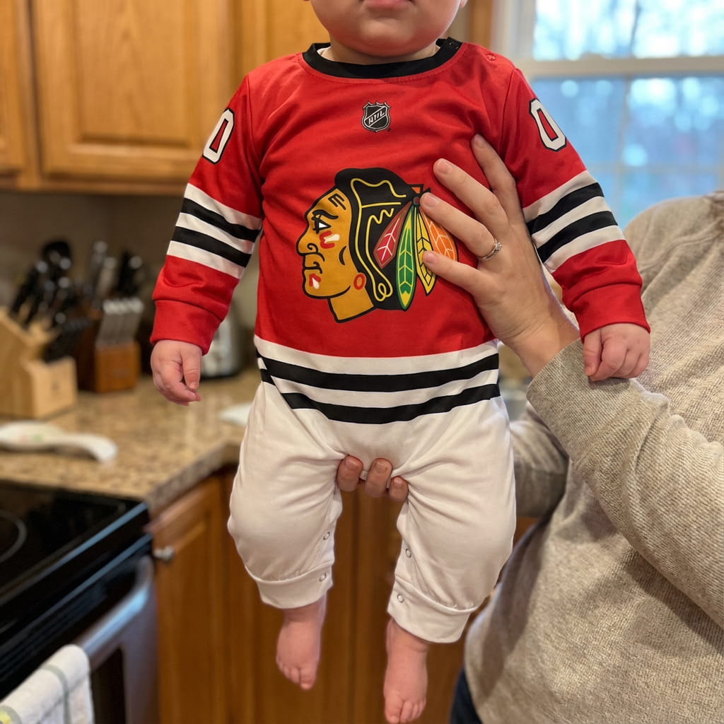 Baby Wearing Chickago Blackhawks Baby Onsie Jumpsuit Held By Their Mother
