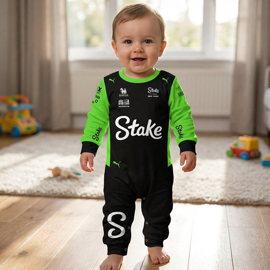 Baby standing wearing Stake Kick 2025 F1 jumpsuit onesie smiling in playroom black green racing romper