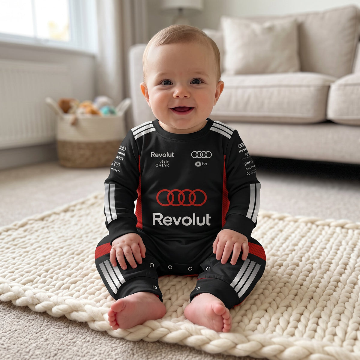 Baby sitting on blanket wearing Audi 2026 racing onesie smiling with Audi rings and Revolut logo