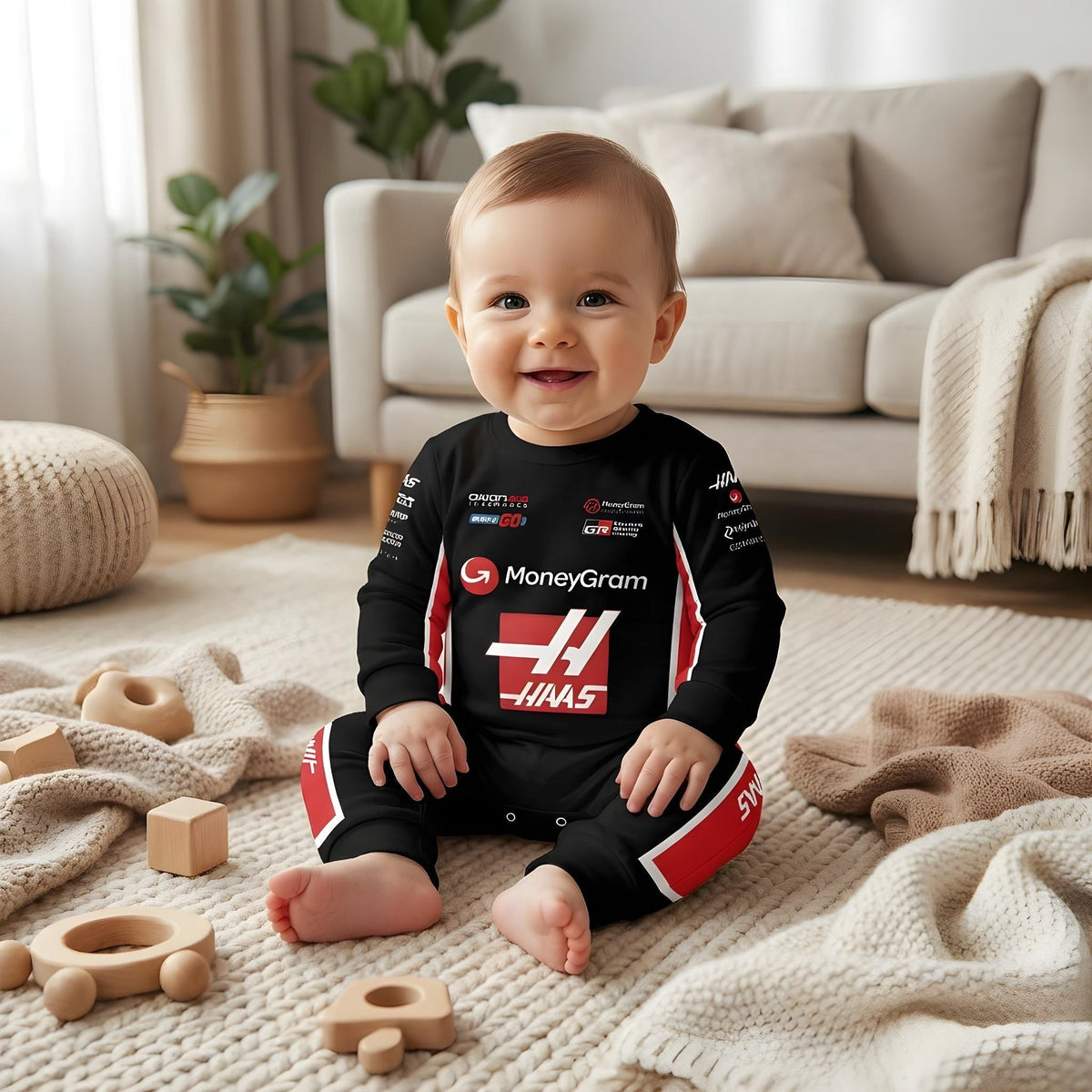 Baby sitting in Haas 2025 F1 baby onesie smiling on blanket with wooden toys in living room