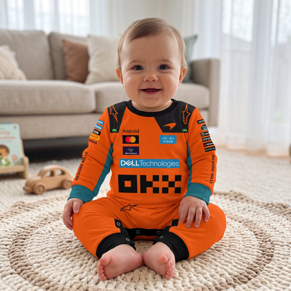 Baby sitting in McLaren 2026 racing onesie jumpsuit orange F1 team design with OKX and Dell logos on rug