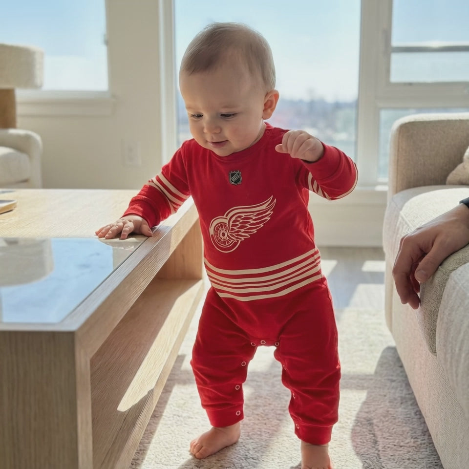 Baby taking first steps whiule wearing a detroit red wings hockey baby onesie jumpsuit