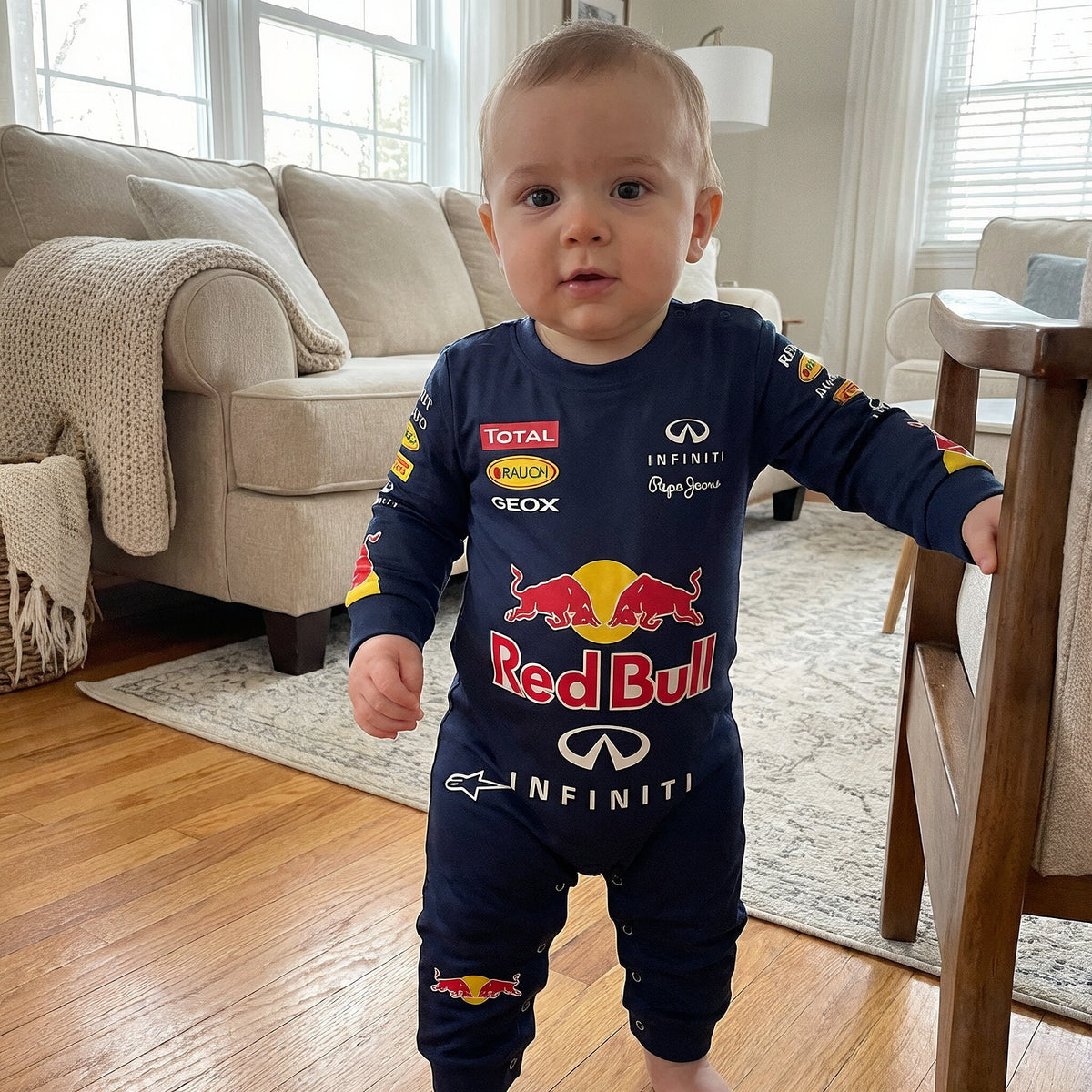 Toddler wearing Red Bull Vettel era racing onesie jumpsuit standing in living room holding chair