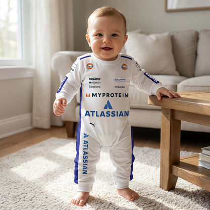 Baby standing wearing Williams 2025 F1 jumpsuit onesie smiling in living room with Atlassian racing print