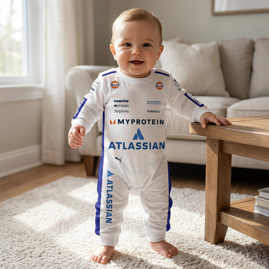 Baby standing wearing Williams 2025 F1 jumpsuit onesie smiling in living room with Atlassian racing print