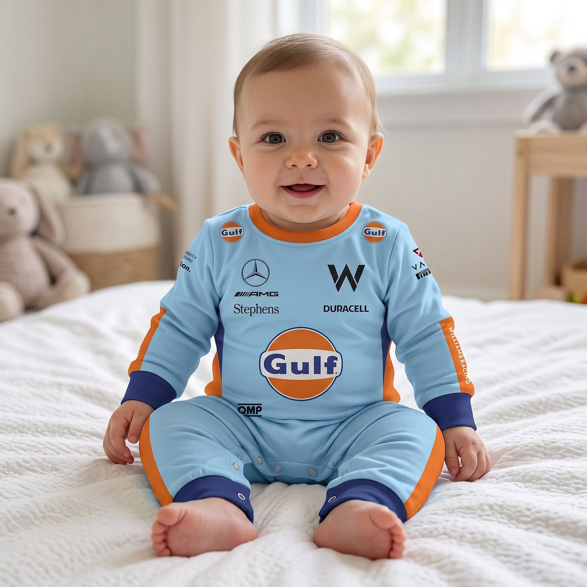 Baby sitting on bed wearing Williams Gulf special edition racing onesie jumpsuit smiling in nursery