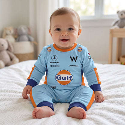 Baby sitting on bed wearing Williams Gulf special edition racing onesie jumpsuit smiling in nursery